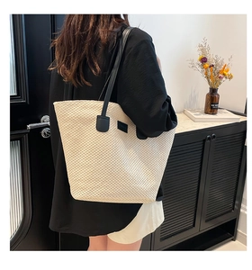 Detail of straw woven tote bag with black leather straps and decorative label on model
