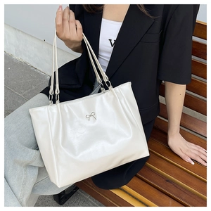 Close-up of cream glossy leather tote with silver bow pendant and double straps