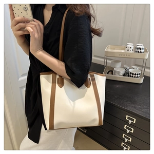 Detail of minimalist cream tote bag with brown leather handles worn by a model