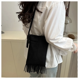 Detail of a black suede crossbody bag featuring elegant long fringe and quilted texture