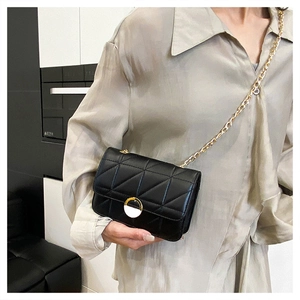 Detail of black quilted shoulder bag with gold chain strap and circular buckle