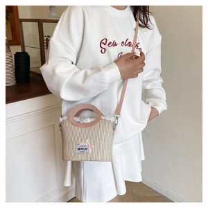 Detail of a straw mini bucket bag with pink leather handle and delicate white lace trim