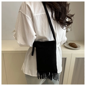 Rear view of model wearing a minimalist black fringe crossbody bag with long tassels
