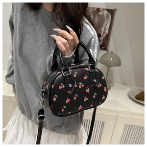 Detail of black oval crossbody bag with red cherry print and adjustable shoulder strap