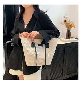Detail of a woven paper straw bucket bag with black leather handles and a fashion patch