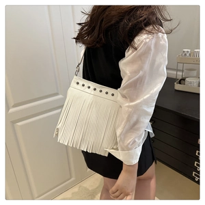 Vista detallada del bolso de hombro en cuero blanco con flecos y tachuelas en modelo