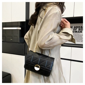 Detail of a black quilted crossbody bag with a gold chain strap on a model's shoulder