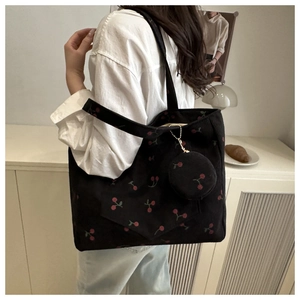 Détail du sac fourre-tout en velours noir avec broderie cerise et vue latérale sur l'épaule
