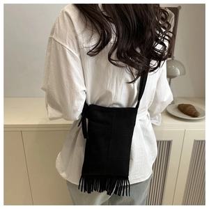 Macro shot of black suede fringe crossbody bag worn by model over a white shirt