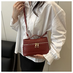 Detail of dark red woven texture on crossbody bag with gold zippers and leather handle