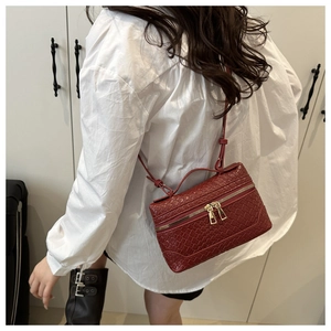 Detail of dark red woven texture tote bag featuring golden double zipper and adjustable strap
