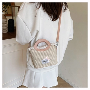 Détail d'un sac seau en paille avec poignées en cuir rose et bordure en dentelle blanche