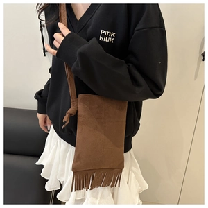Detail view of brown suede crossbody bag featuring long fringe tassels and knotted strap
