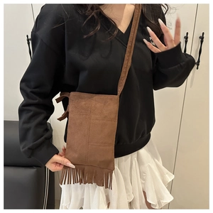 Close-up of brown suede crossbody bag with fringe tassels and stitching details