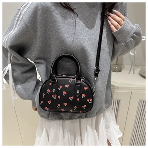Detail of black mini PU leather handbag with red cherry print and silver buckles