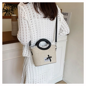 Detail of straw bucket bag featuring white lace trim and black bow decoration