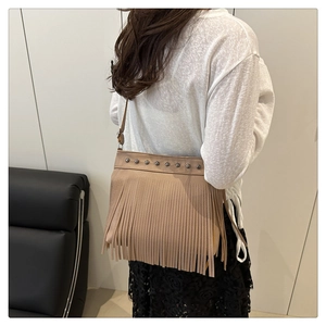 Detailed view of metallic studs and flowing fringe on the light brown bucket bag