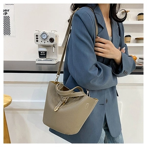 Close-up of khaki litchi grain bucket bag with belt buckle and adjustable shoulder strap