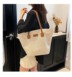 Close-up of a large straw tote bag with brown leather handles worn by a model