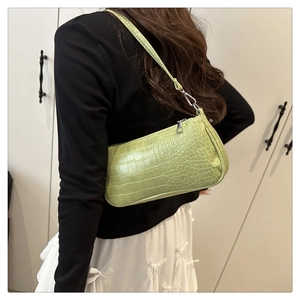 Détail du sac baguette vert clair à motif crocodile porté par un mannequin à l'épaule