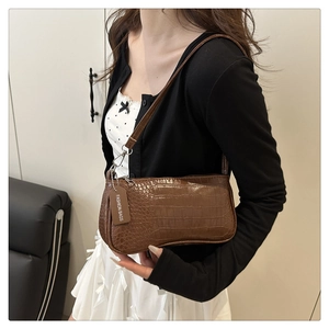 Détail de la texture crocodile sur un sac baguette en cuir brillant marron foncé
