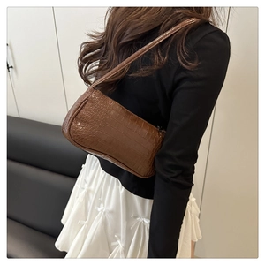 Sac baguette marron à motif crocodile porté à l'épaule sur une tenue blanche
