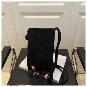 Detail of black suede crossbody bag with long fringes on a vintage chair