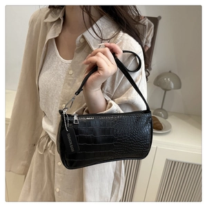 Détail d'un sac baguette noir à motif crocodile porté par un mannequin en intérieur