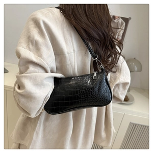 Détail du sac baguette noir à motif crocodile porté à l'épaule pour un style rétro