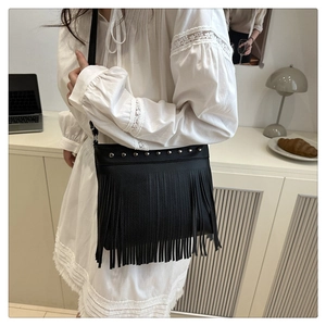 Detail of black faux leather bucket bag with silver studs and long tassels on white dress