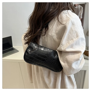 Gros plan du sac baguette noir à motif crocodile avec longue bandoulière sur l'épaule