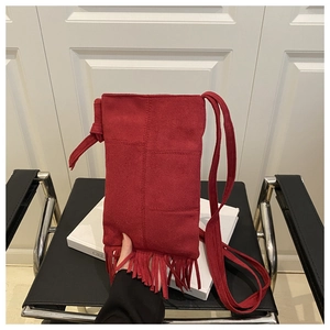 Macro shot of red suede mini bag featuring long tassels on a stylish leather chair