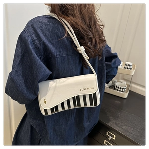 Detail of piano key design on cream shoulder bag with music note emblem and strap