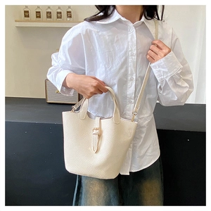 Close-up of creamy white lychee grain leather bucket bag with metal buckle on a model