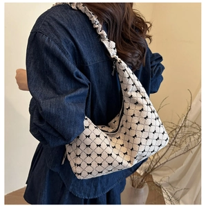 Detail of beige plaid canvas shoulder bag featuring black bow embroidery and ruched strap