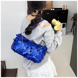 Blue sequin crescent bag with chain strap shown on model in a modern interior setting