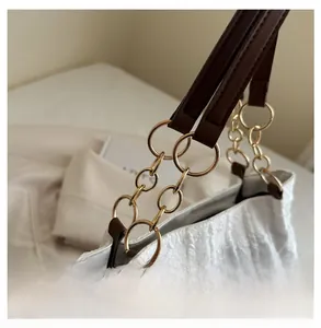 Detail of white pleated shoulder bag featuring gold chain hardware and brown strap