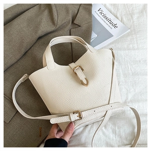 Close-up of beige lychee leather bucket bag featuring gold buckle and adjustable strap