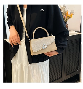 Detail of beige crossbody bag featuring shimmering flap and heart-shaped metal clasp