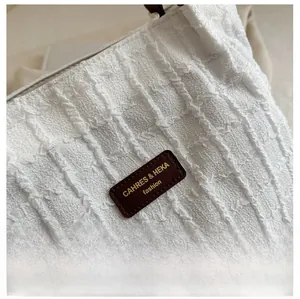 Detailed close-up of white bubble pleated fabric and leather brand tag on tote bag