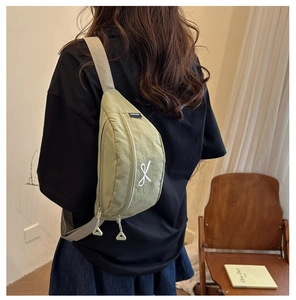 Detail of light green nylon crossbody bag showing the bow embroidery and adjustable strap