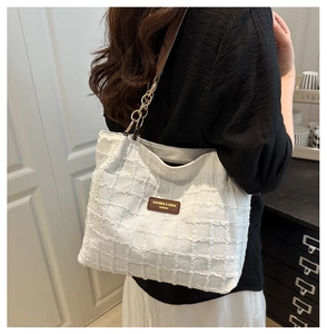 Close-up of beige tweed tote bag with leather logo patch and gold chain strap detail