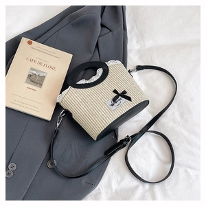 Détail d'un sac seau en paille tressée avec bordure en dentelle blanche et nœud noir