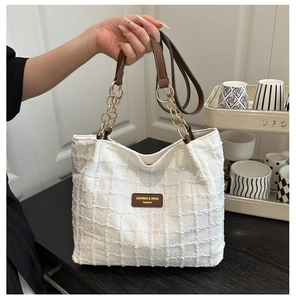 Detail of white waffle texture tote bag with brown leather strap and gold chain link
