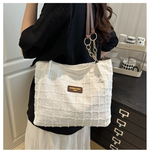 Detailed view of white checkered tote bag with brown leather strap and chain