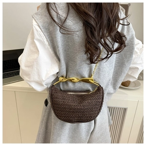 Detail of a brown woven crescent bag with gold twisted metal handle and chain strap