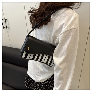 Detail of piano pattern shoulder bag with golden musical note emblem and striped design