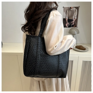 Close-up of black woven texture leather tote bag worn by a model in a minimalist setting