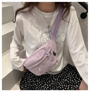 Détail du sac bandoulière en toile violet clair avec broderie nœud blanc sur un modèle