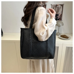Close-up of a large black woven tote bag with checkerboard pattern on a shoulder model